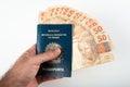 Hand holding Brazilian passport with fifty reais banknotes. Brazilian money