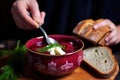 hand holding bread slice on side of borscht bowl