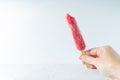 Hand holding a bright red icy popsicle with a bit taken out of it and a white background with copy space Royalty Free Stock Photo