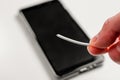 Hand holding a broken torn charger cable with a black smartphone on a white background Royalty Free Stock Photo