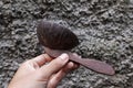 The hand holding a brown wooden rice ladle, with a wall in the background