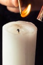 Hand holding burning match stick lighting candle on black background. Match with the flame and candle in dark room close up Royalty Free Stock Photo