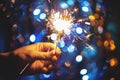 Hand holding a burning sparkler firework on Christmas light bokeh background.