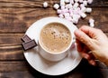 Hand holding cap of coffee on small plate with two small chocolate and marshmallow on the table.  Flat Lay with no people Royalty Free Stock Photo