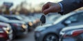 Hand holding car keys with dealership cars in background. Close-up shot in the evening light Royalty Free Stock Photo