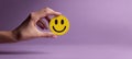 The hand holding a cheerful yellow smiley face on a purple background. AI generated image Royalty Free Stock Photo
