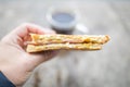 Hand holding a cheese and ham sandwich in front of a blurry cup of coffee Royalty Free Stock Photo