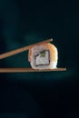 Hand holding chopstick to eat Sushi on dark background, vertical