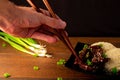 Chopsticks reaching for beef strips and rice on a wooden table. Black backdrop.