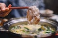 Hand holding chopsticks with ripe Kurobuta Pork in Shabu Shabu and Sukiyaki hot pot. Food concept with gourmet Japanese hot pot