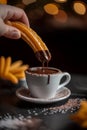 A hand holding a churro thatÃ¢â¬â¢s dripping with chocolate, being dipped into a white cup filled with hot melted chocolate