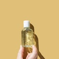 Hand holding clear plastic bottle with white cap on solid yellow background Royalty Free Stock Photo