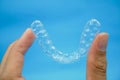 Hand holding clear plastic retainer teeth that isolated on blue sky background. it`s an equipment for orthodontist give the