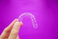 Hand holding clear plastic retainer teeth that isolated on purple background. it`s an equipment for orthodontist give the patien