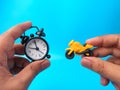 Hand holding clock and motorcycles toys on a blue background