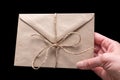 Hand holding closed brown craft envelope tied with twine isolated on black background. An envelope for your Royalty Free Stock Photo