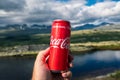 Hand holding a Coca Cola can towards beautiful mountain scenery outdoors in the norwegian wilderness