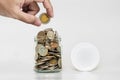 Hand holding coin with jar glass full of coins, and jar cap with copy space Royalty Free Stock Photo