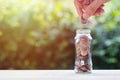 Hand holding coin over coins in glass jar on wood table Royalty Free Stock Photo