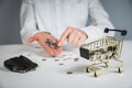 Hand holding a coin with pile of coin in the shopping cart on white and grey background