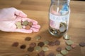 Hand holding coins and a jar next to it labeled travel with euro money inside and coins outside on top of a wooden table. Royalty Free Stock Photo