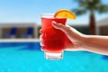 hand holding a cold glass of fruit punch by the pool