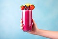 hand holding a colorful berry smoothie against a bright backdrop