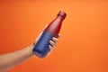 Hand holding a colorful thermal bottle on an orange background