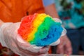 Hand holding cone of rainbow colored ball of shaved ice