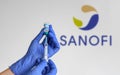 Close-up image of doctor holding covid vaccine vial with sanofi logo in background