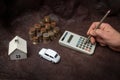 Hand holding a crayon and calculating taxes with model house, car and multiple coin stacks on brown leather background Royalty Free Stock Photo