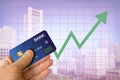 Hand holding credit card from bank with cityscape and green arrow going up showing real estate market economy going up with blurre