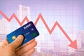 Hand holding credit card from bank with cityscape and red arrow going down showing real estate market economy going down with blur Royalty Free Stock Photo