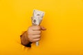 Hand holding crumpled money through hole in yellow paper wall Royalty Free Stock Photo