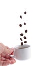 The hand holding cup of coffee with falling beans on white. Royalty Free Stock Photo