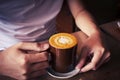 hand holding cup of coffee top view surface heart shape in wooden background