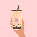 Hand holding a cup of famous Taiwanese bubble tea on pink background. Take away glass with sticker of pearl milk tea