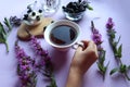 Hand holding a Cup of tea against the background of a morning Breakfast of blackberries and a bouquet of flowers, close-up, top