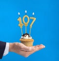 Hand delivering birthday cupcake - Candle number 107 on blue background