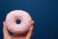 Hand holding a delicious colorful pink donut with sprinkles near dark blue background, sugar concept Royalty Free Stock Photo