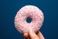 Hand holding a delicious colorful pink donut with sprinkles near dark blue background, sugar concept Royalty Free Stock Photo