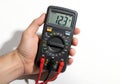 Hand holding a digital multimeter displaying 12.3 volts on a white background {Ai generated Royalty Free Stock Photo