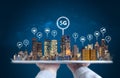 Hand holding digital tablet with modern buildings hologram and technology icons. Smart city, 5g, internet and networking technolog Royalty Free Stock Photo