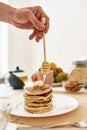 Hand holding dipper, adding honey on top of stack of sweet tasty pancakes