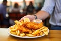 hand holding a dish of fish and chips in a cafe setting Royalty Free Stock Photo