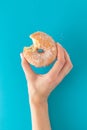 Hand holding a doughnut with a bite, on blue background