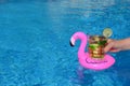 Hand holding a drink in an inflatable pink flamingo drinks holder in swimming pool