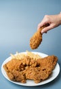 Hand holding drumsticks, crispy fried chicken with french fries in white plate  on blue background Royalty Free Stock Photo