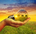 Hand holding eco light bulb with wind turbines at sunset. Royalty Free Stock Photo