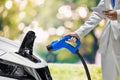 Hand holding Electric car charger. Electric Vehicle EV Charging station on blurred nature with soft light background.  Air polluti Royalty Free Stock Photo